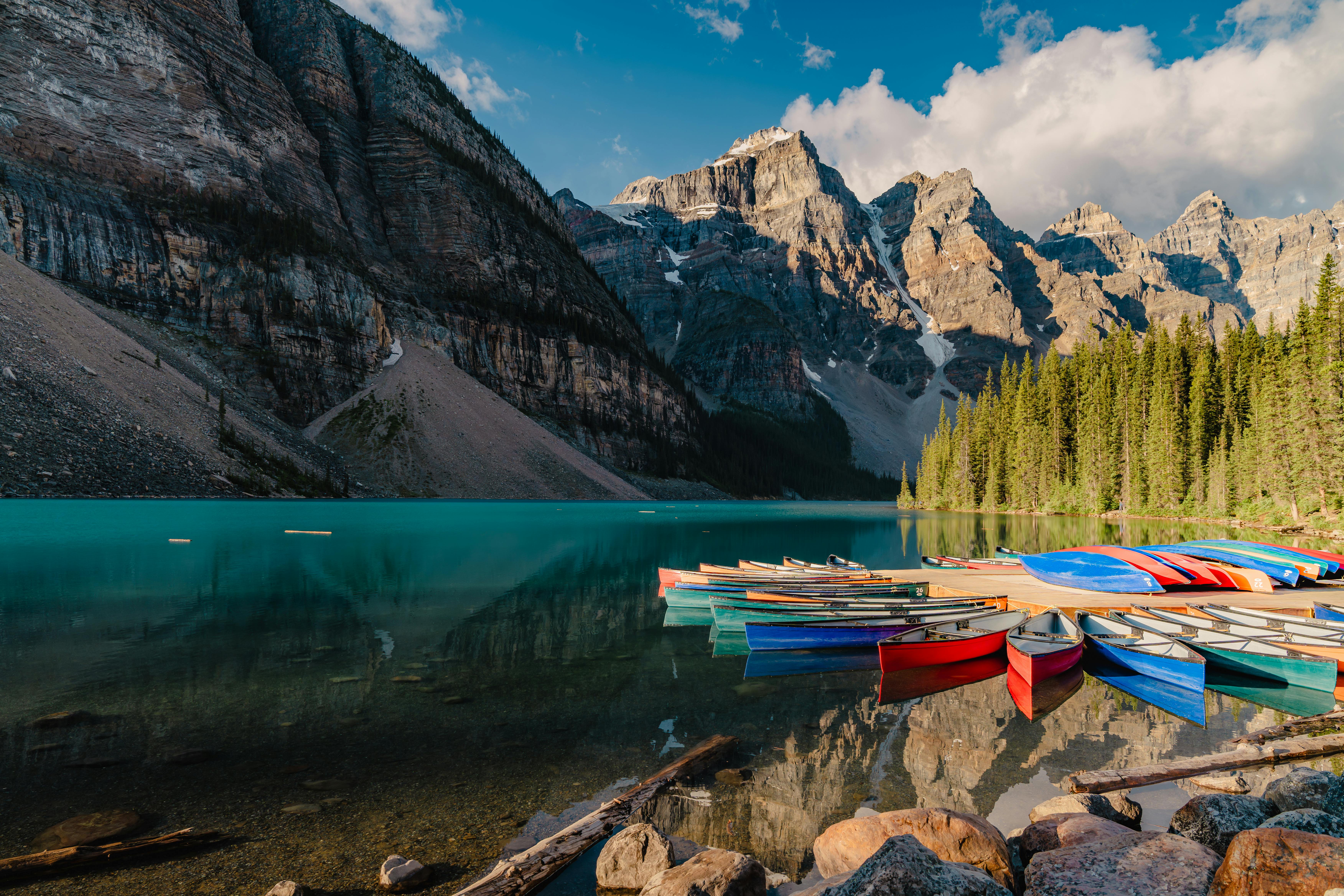 Stunning view of colorful canoes at Moraine Lake with majestic mountains and evergreen trees in the background.