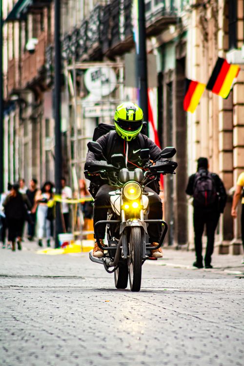 Free A motorcyclist wearing a green helmet rides through a cobblestone street in Puebla, México, capturing urban life. Stock Photo