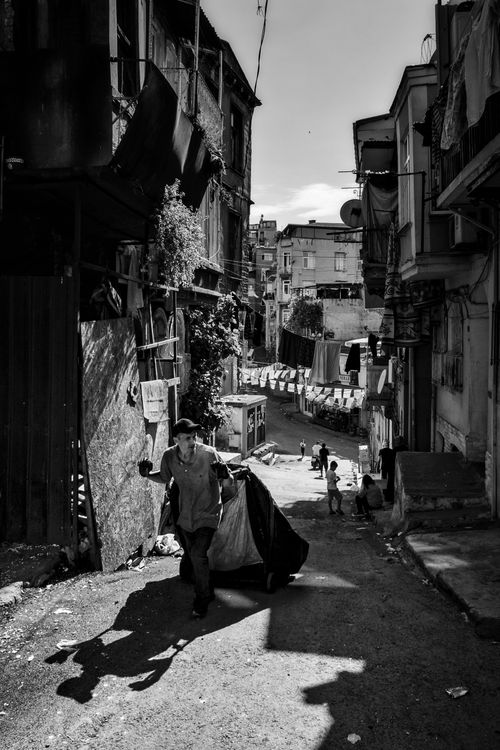 Free Black and white urban alleyway with a man carrying a large bag, showcasing city life. Stock Photo