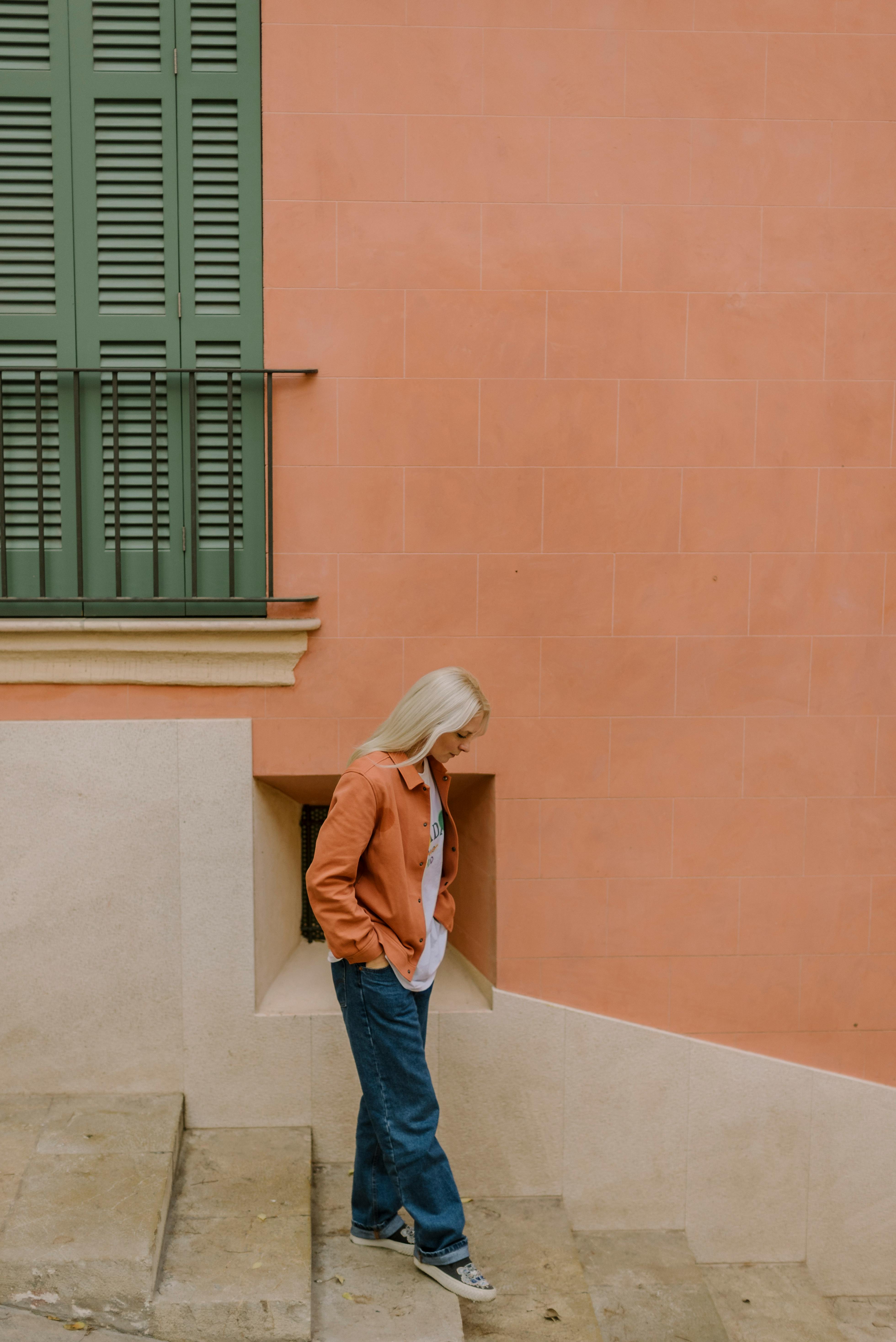 A woman in a casual outfit walks down city steps against a peach wall. Urban street photography.