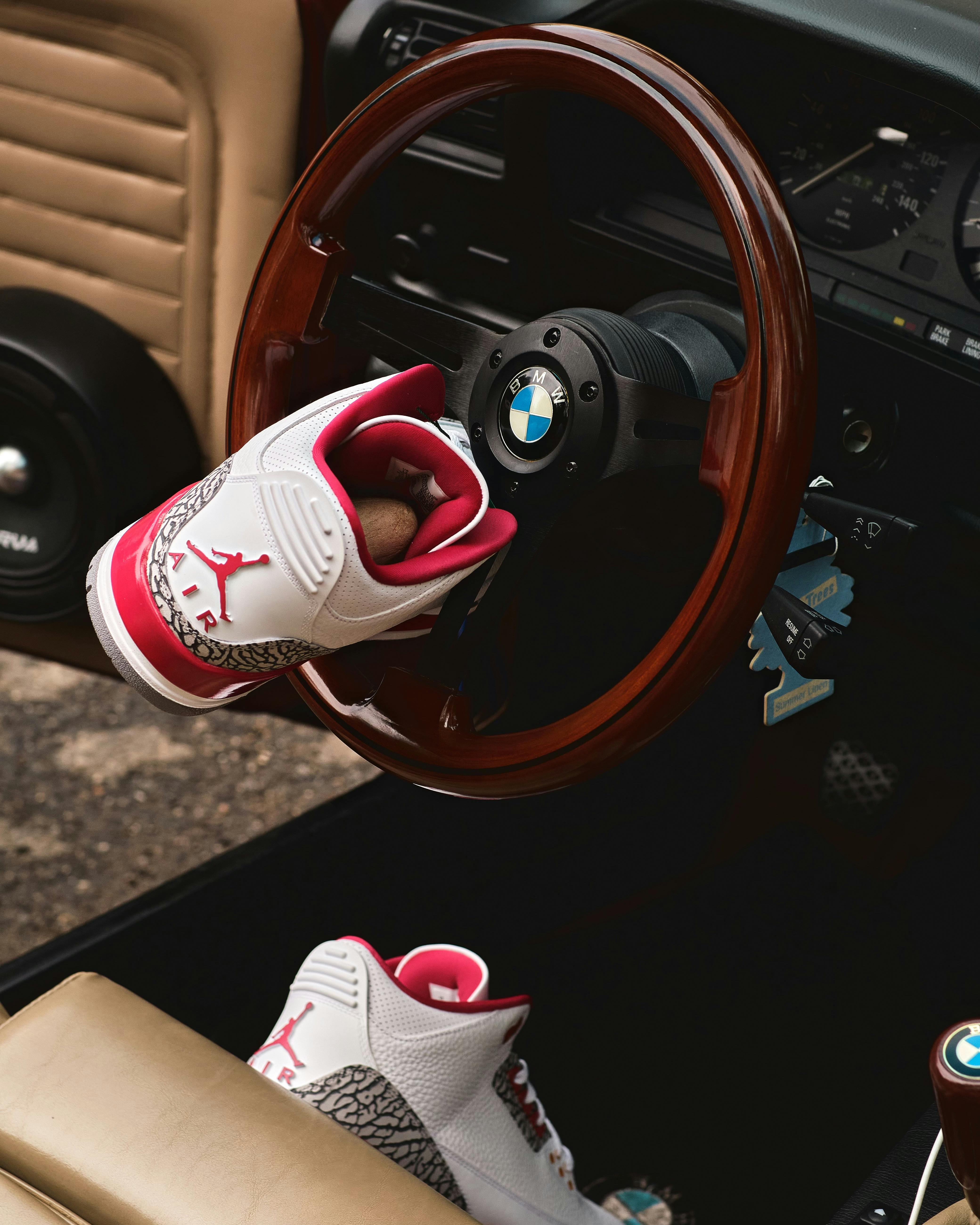 Stylish sports sneakers hanging on a classic BMW steering wheel interior.