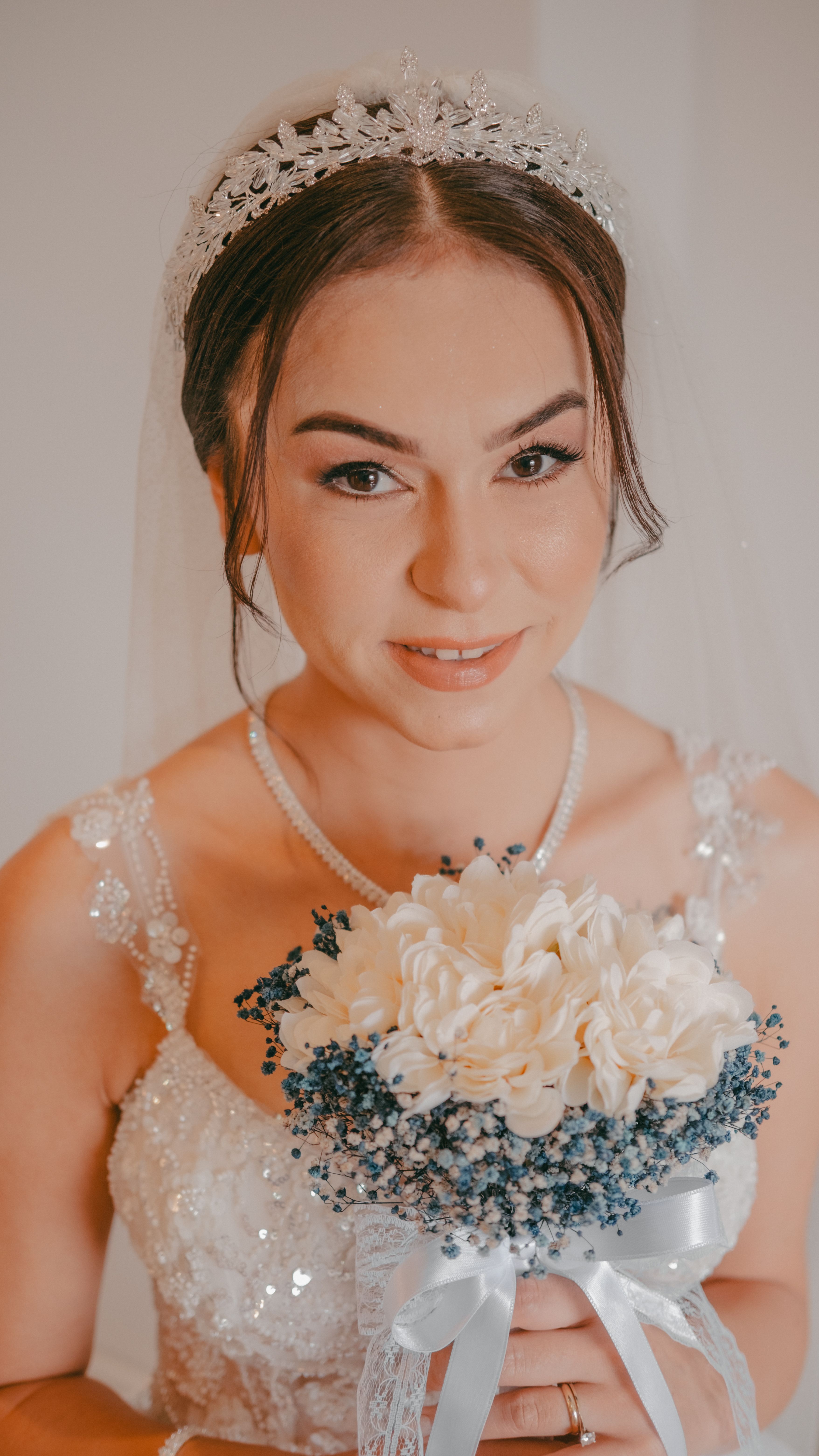 Bride in a stunning wedding gown holding a delicate bouquet with blue and white flowers.