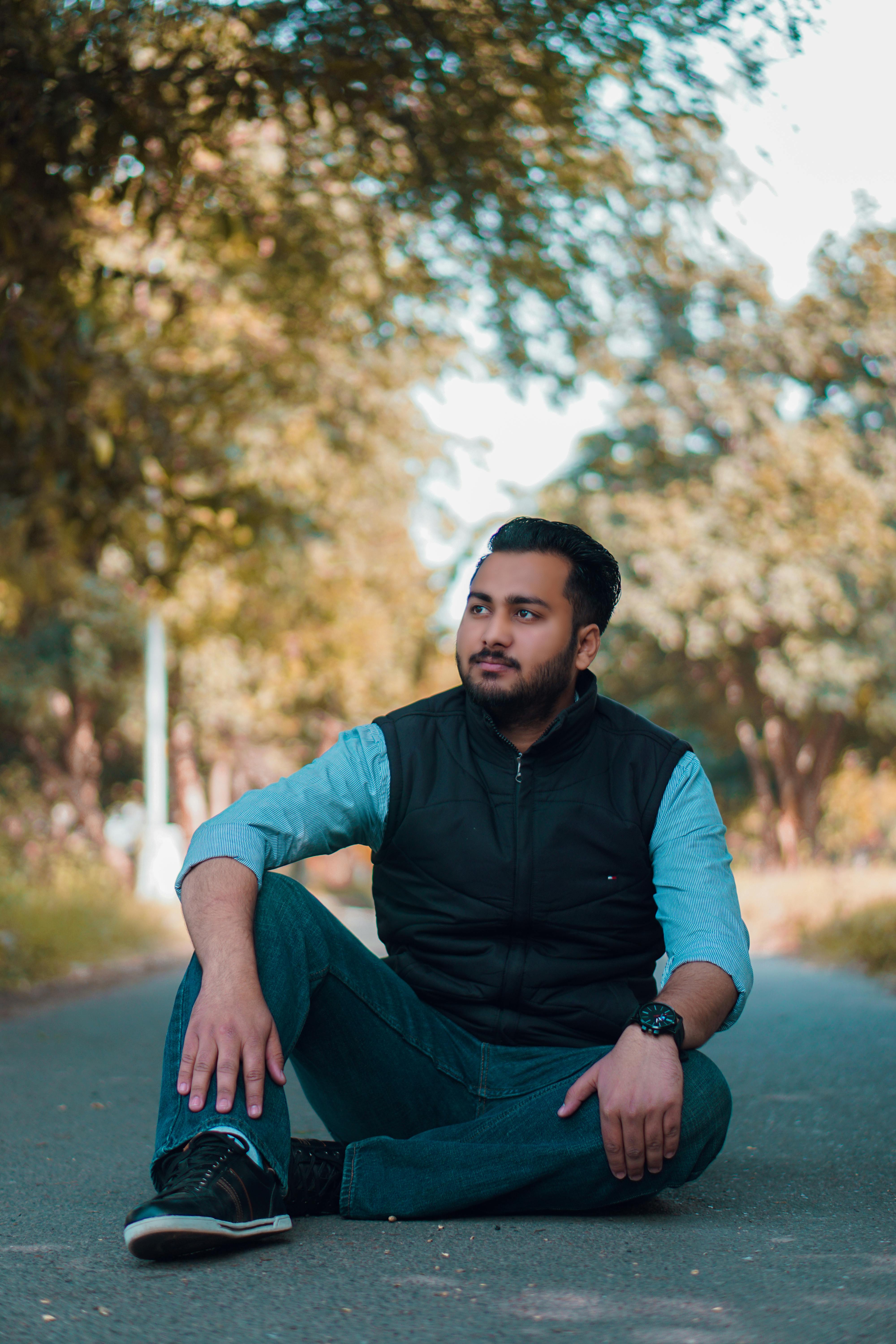 A young man poses casually on an outdoor road, wearing jeans and a jacket.