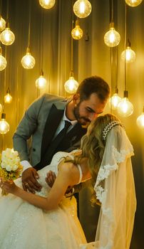 Bride and groom sharing a romantic moment beneath glowing vintage light bulbs.
