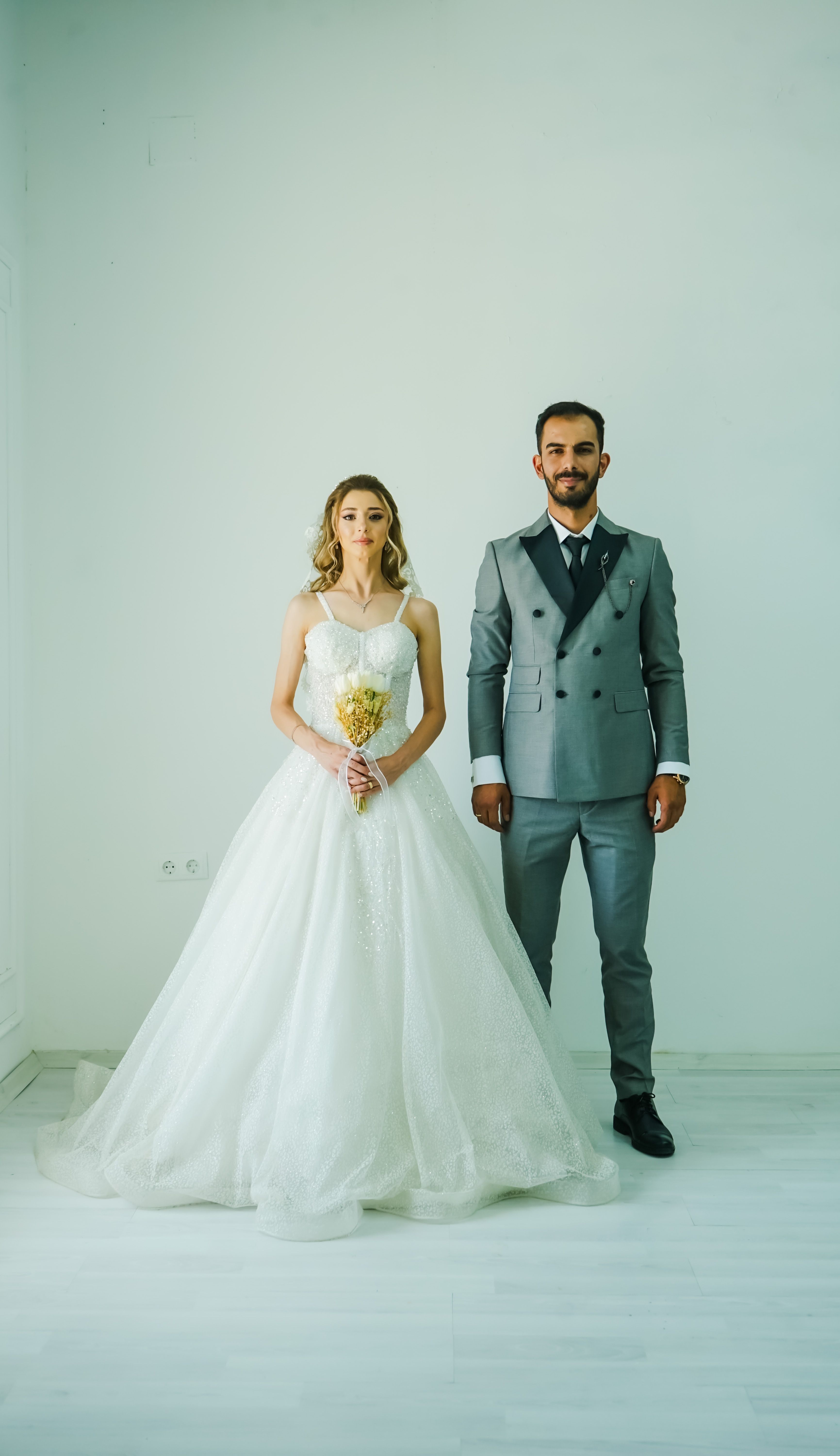 A bride in a white dress and groom in a suit posing indoors on their wedding day.