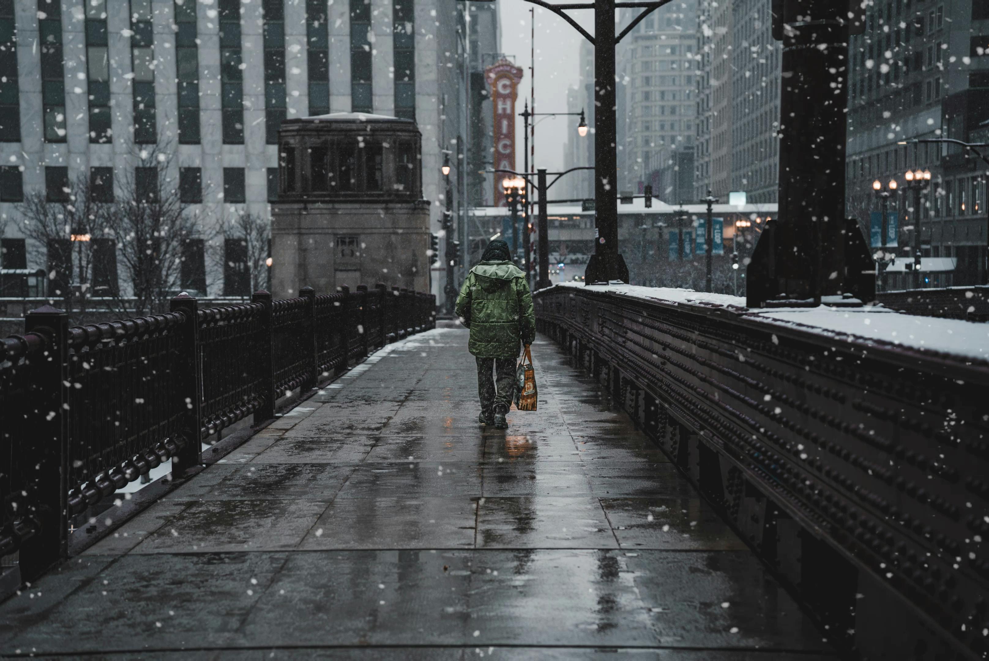 Lonely figure walks through snowy streets of Chicago during winter, capturing urban solitude.
