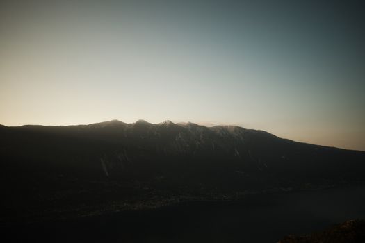 Serene view of Lake Garda with mountains at sunset, showcasing dramatic lighting and natural beauty.