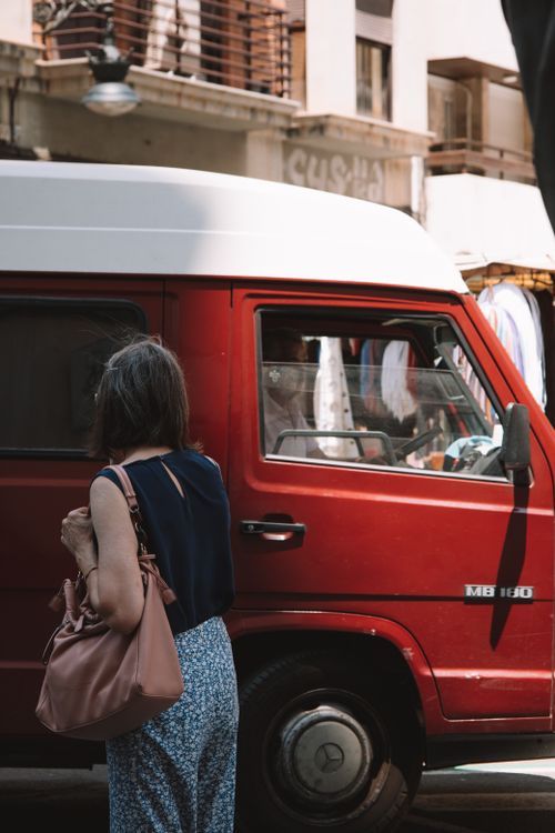 Free A woman with a handbag stands near a red van on an urban street in Valencia, Spain. Stock Photo
