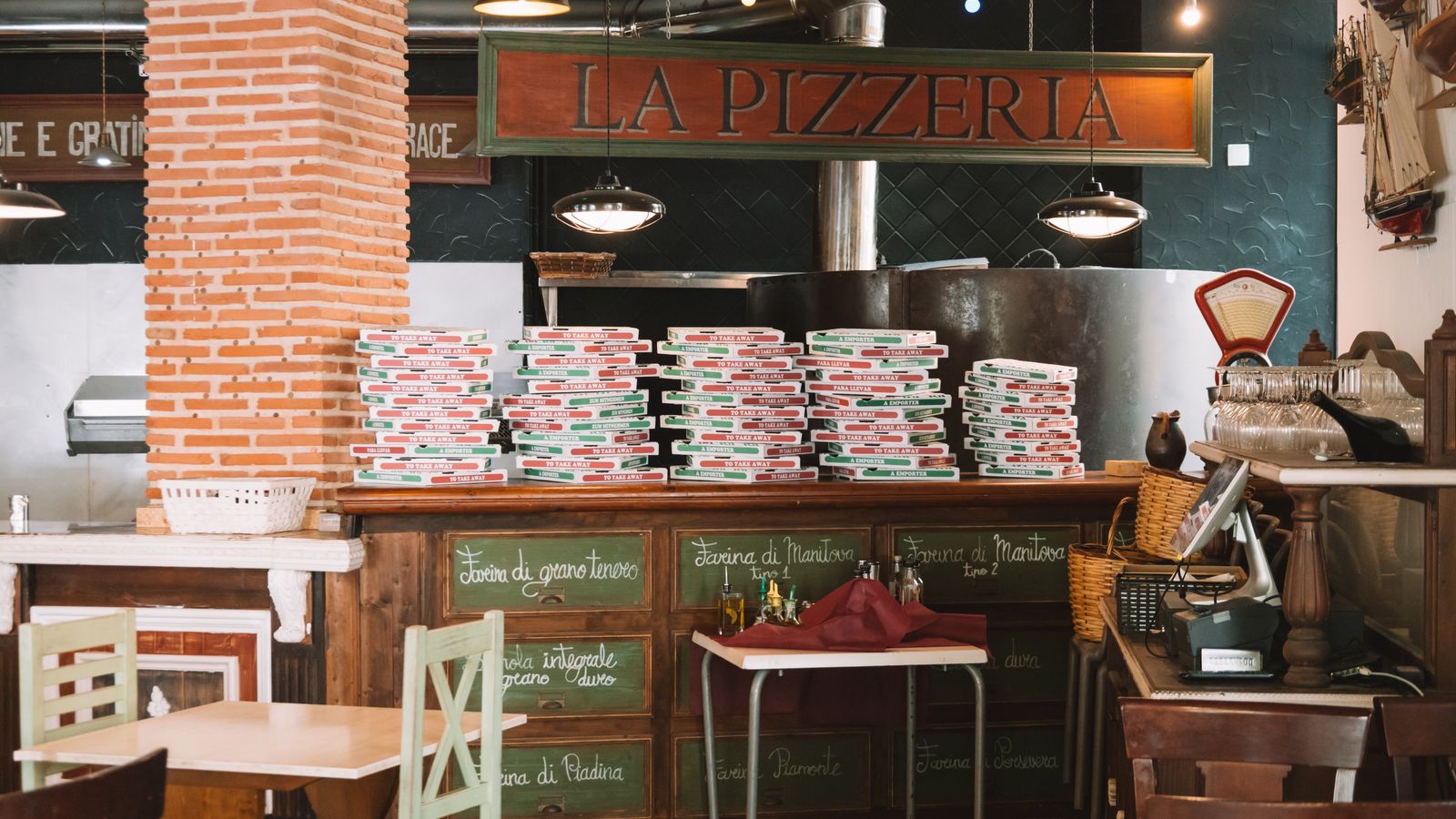 Stacked pizza boxes on the counter of a pizzeria in Valencia, Spain, a real free-license photo by Joaquin Carfagna, chosen because Minimum Wage is set in a struggling pizza shop. It is not a still from the show and it does not show anyone from the cast