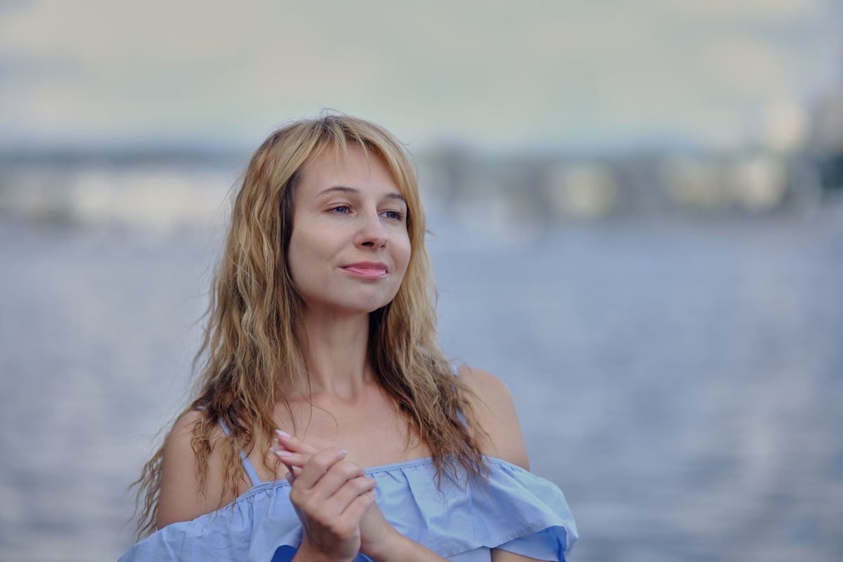 Mujer rubia con el pelo ondulado junto al mar en un ambiente relajado