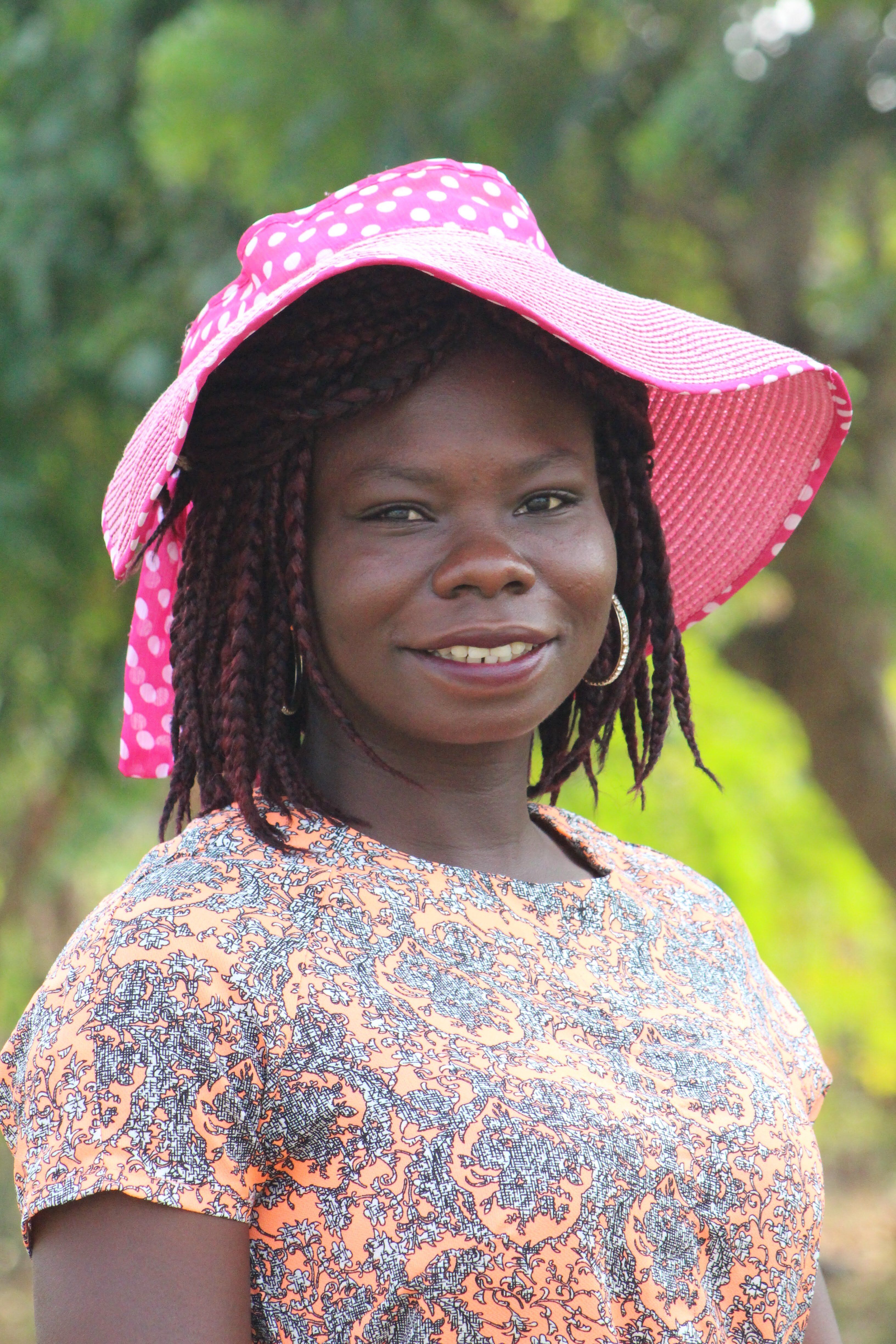 A cheerful woman in a polka dot sun hat smiles outdoors in summer.
