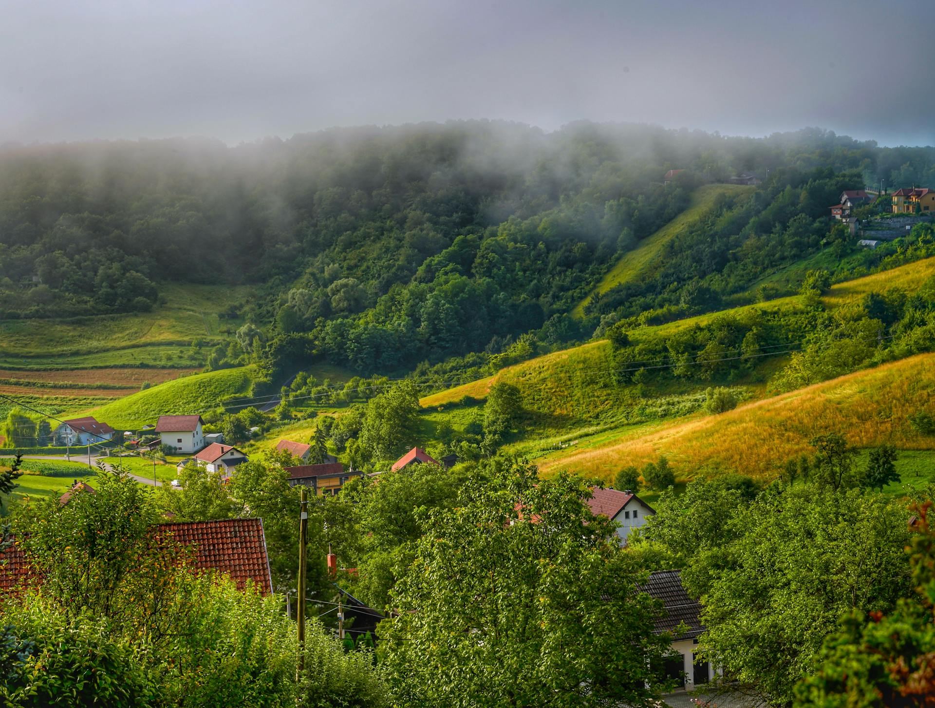 Picturesque rural landscape with foggy hills and lush greenery surrounding quaint village houses.