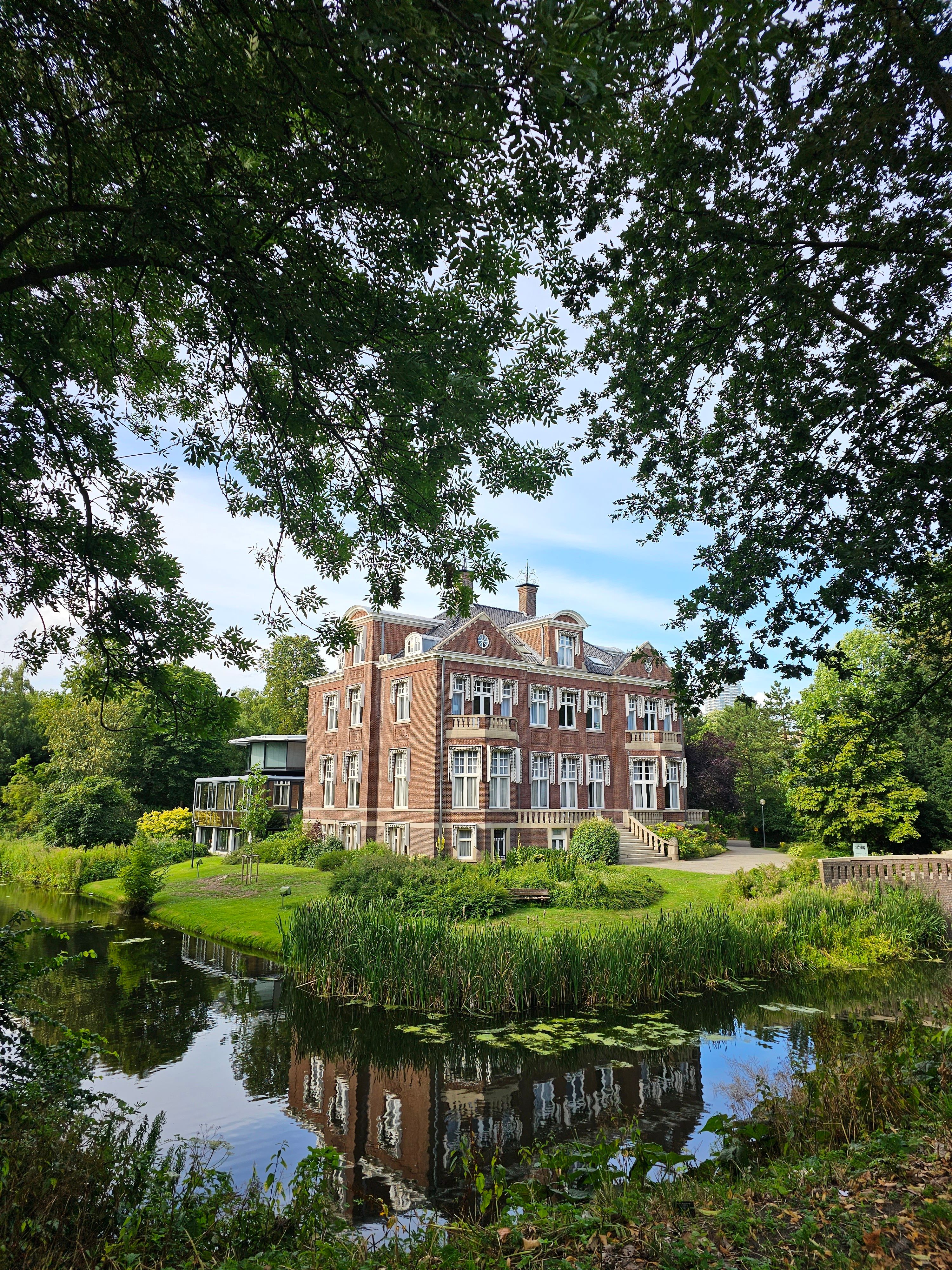 A majestic mansion reflected in a tranquil pond surrounded by greenery and trees.