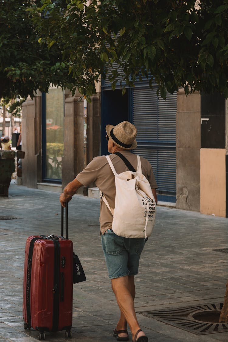 A Man With A Suitcase Walking On The Sidewalk 