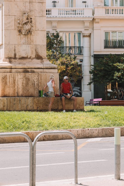 People Sitting under a Monument on a Town Square in Summer 