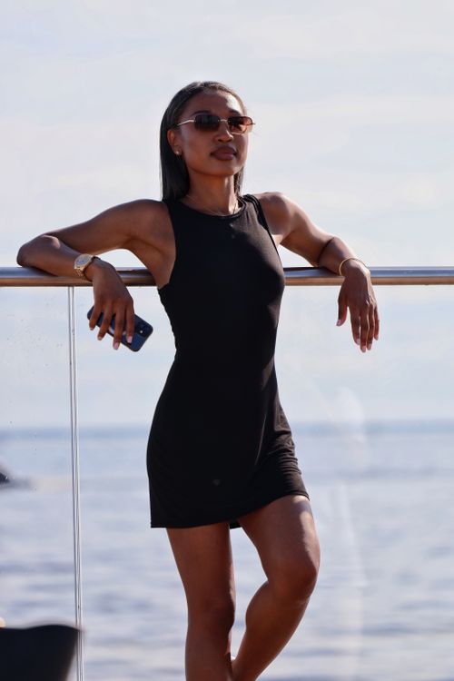 Free Elegant woman in a black dress and sunglasses leaning on a railing by the sea. Stock Photo