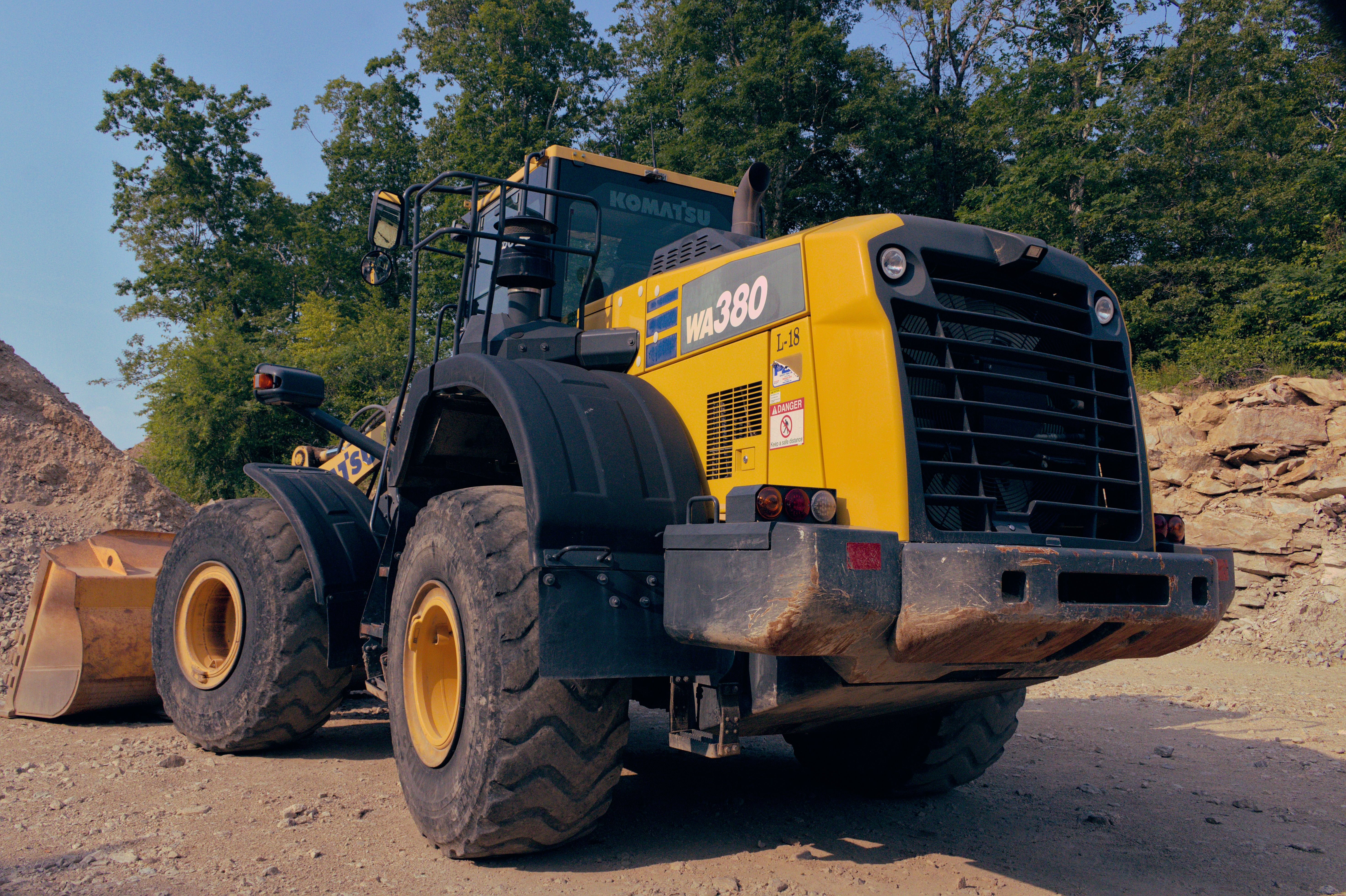 Back view of a yellow bulldozer at a construction site, surrounded by dirt and trees.