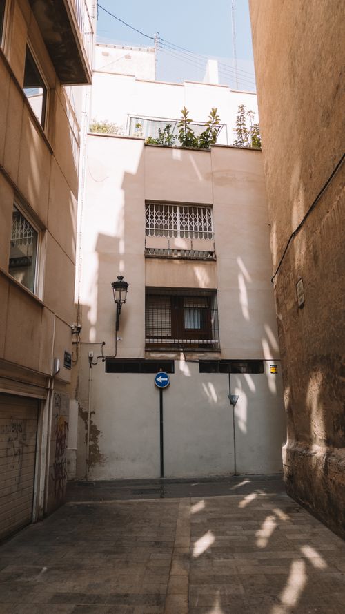 Free A narrow alleyway in Valencia, Spain, showing urban architecture with play of sunlight and shadows. Stock Photo