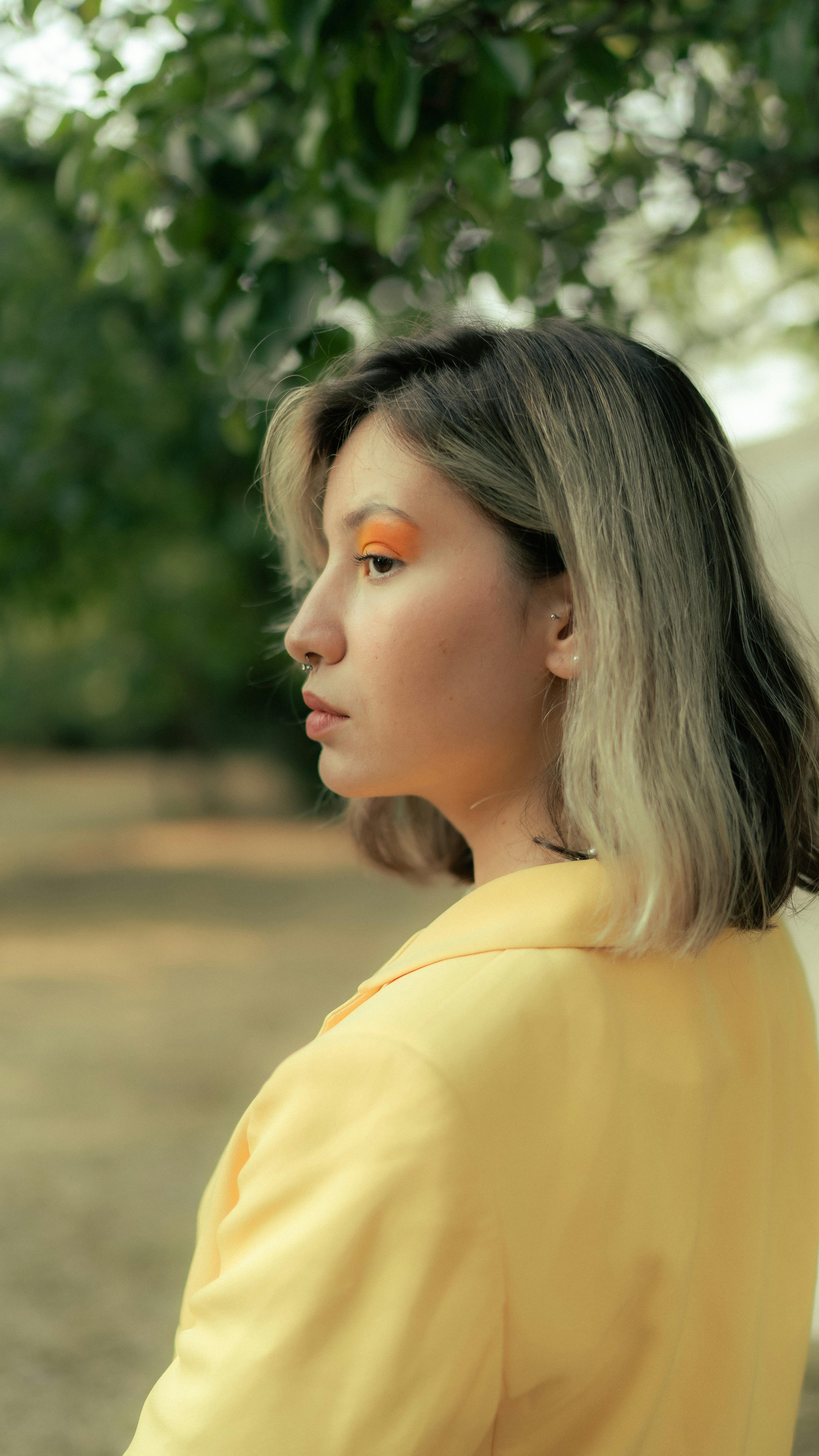 Side profile of a woman with blonde hair in a yellow jacket, captured outdoors.