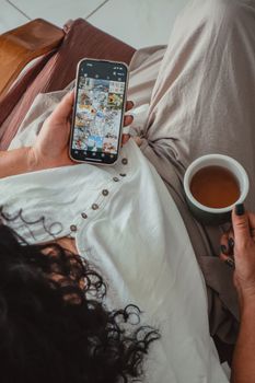 Overhead view of woman holding a smartphone and cup of tea, creating a calm and cozy atmosphere.