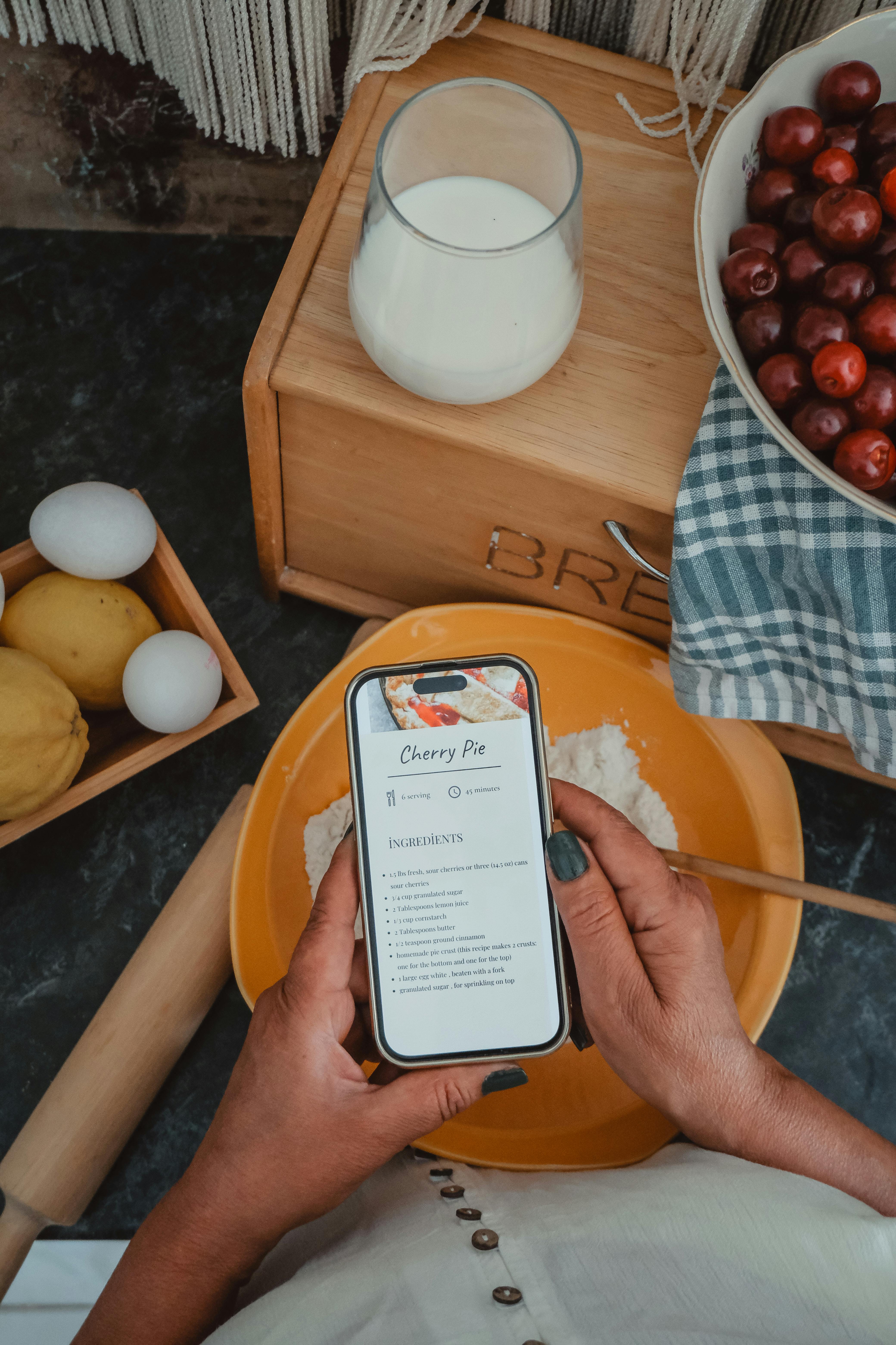 Woman using smartphone to follow cherry pie recipe while baking in kitchen.