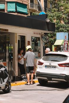 People fueling cars at a sunlit gas station in Valencia, Spain.