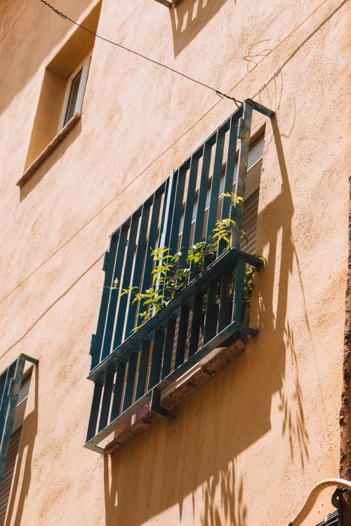 Free Sunlit residential wall in Valencia, Spain featuring a small balcony with green plants. Stock Photo