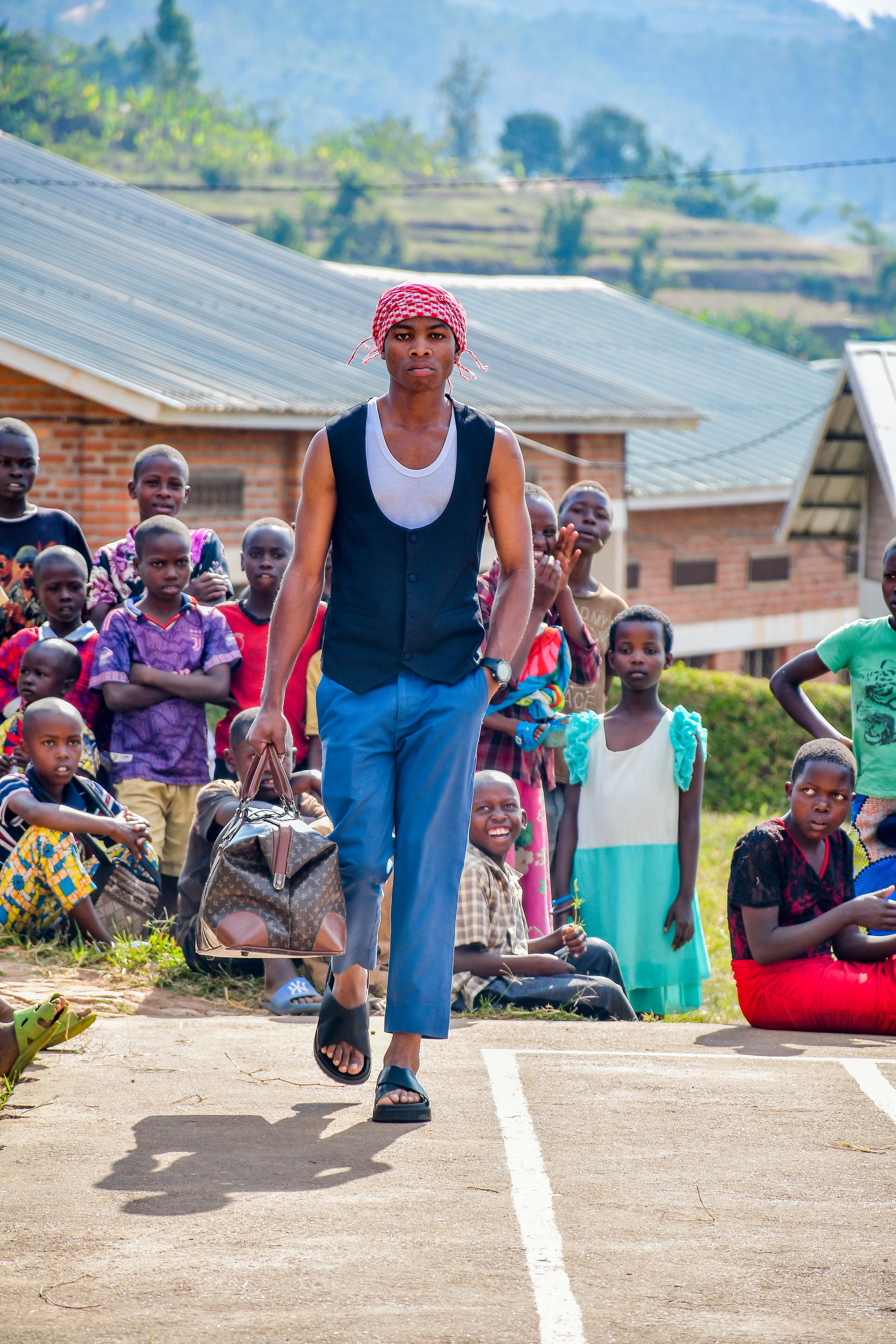 Stylish man with a bag walking in a Kigali village, surrounded by local children.