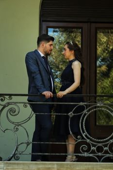 A sophisticated couple in formal attire standing romantically on a balcony during daytime.