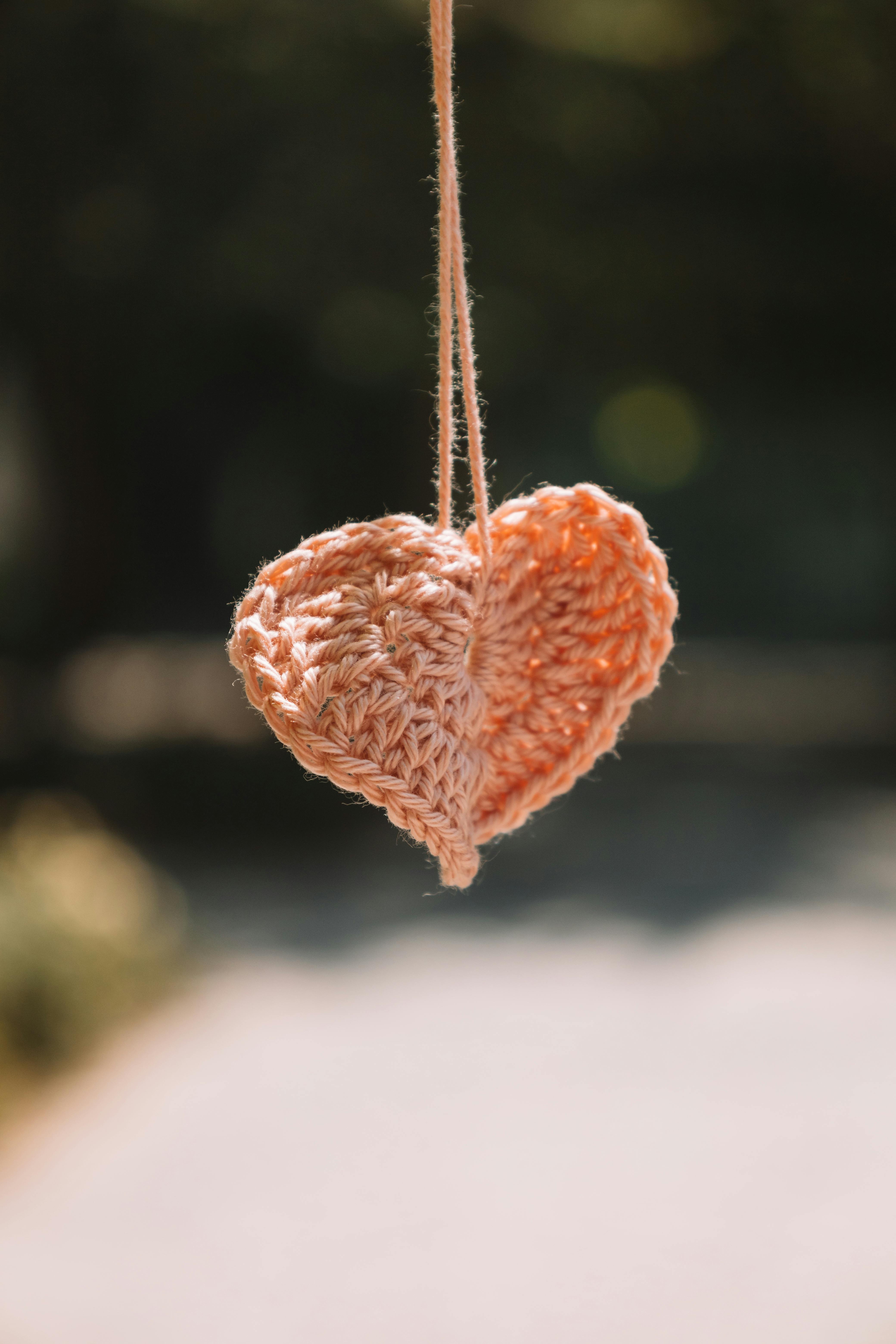 Close-up of a handmade crochet heart decoration hanging outdoors in summer.