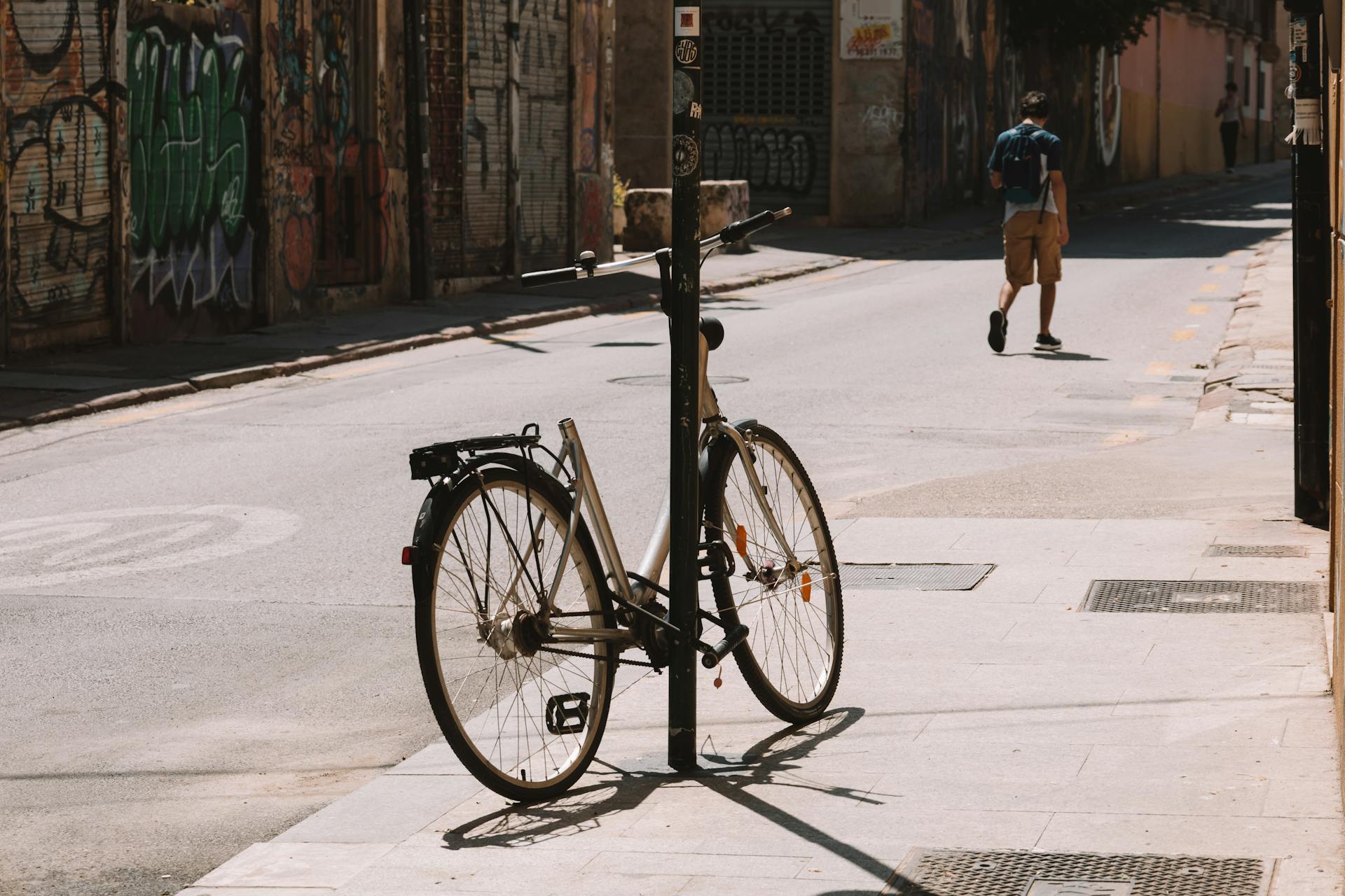 A bicycle locked to a pole on a graffiti-lined street, capturing urban life.