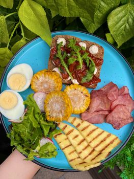 Vibrant breakfast plate featuring corn, toast, eggs, and greens on a blue dish outdoors.