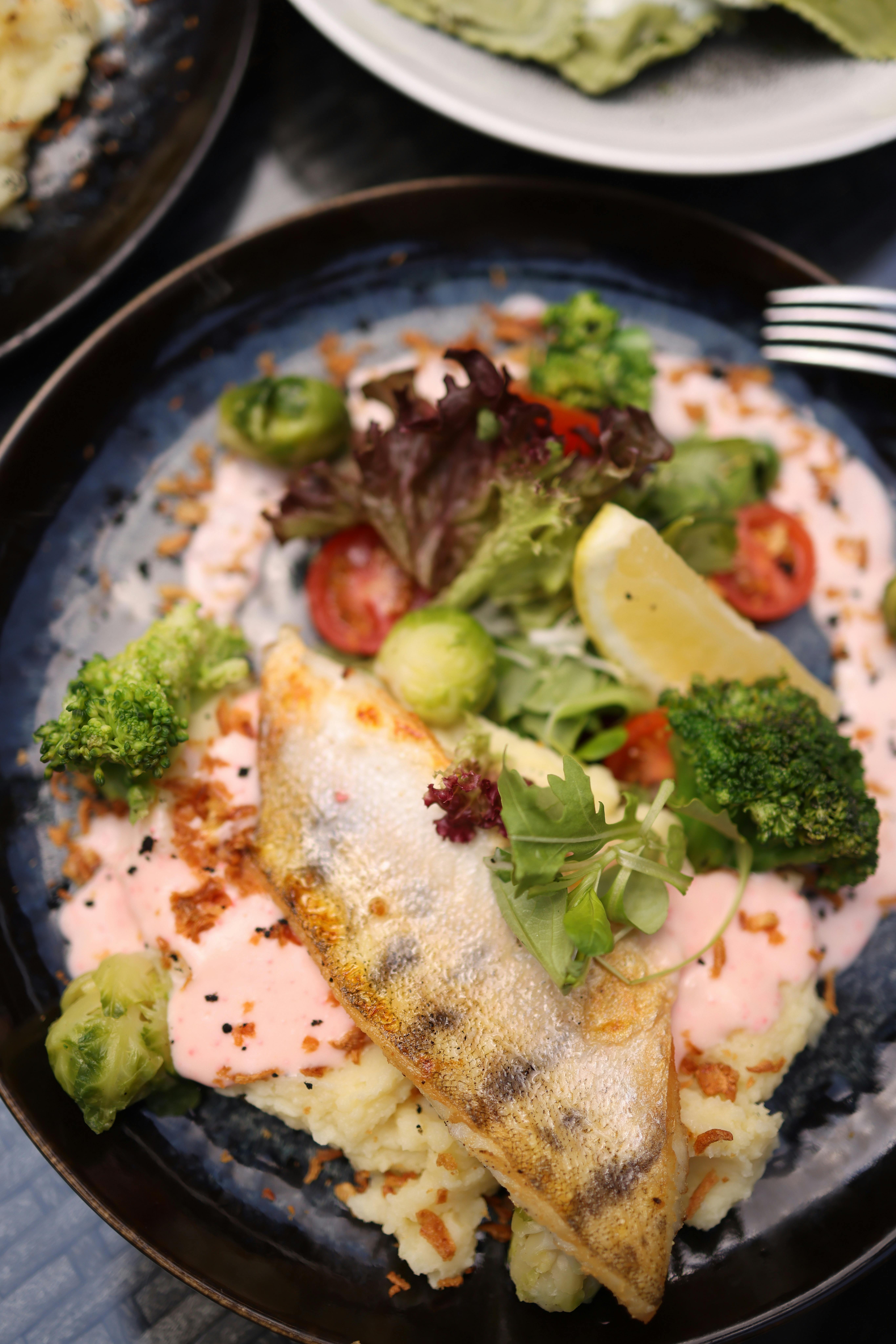 A delicious grilled fish served on a bed of mashed potatoes with fresh vegetables and sauce.