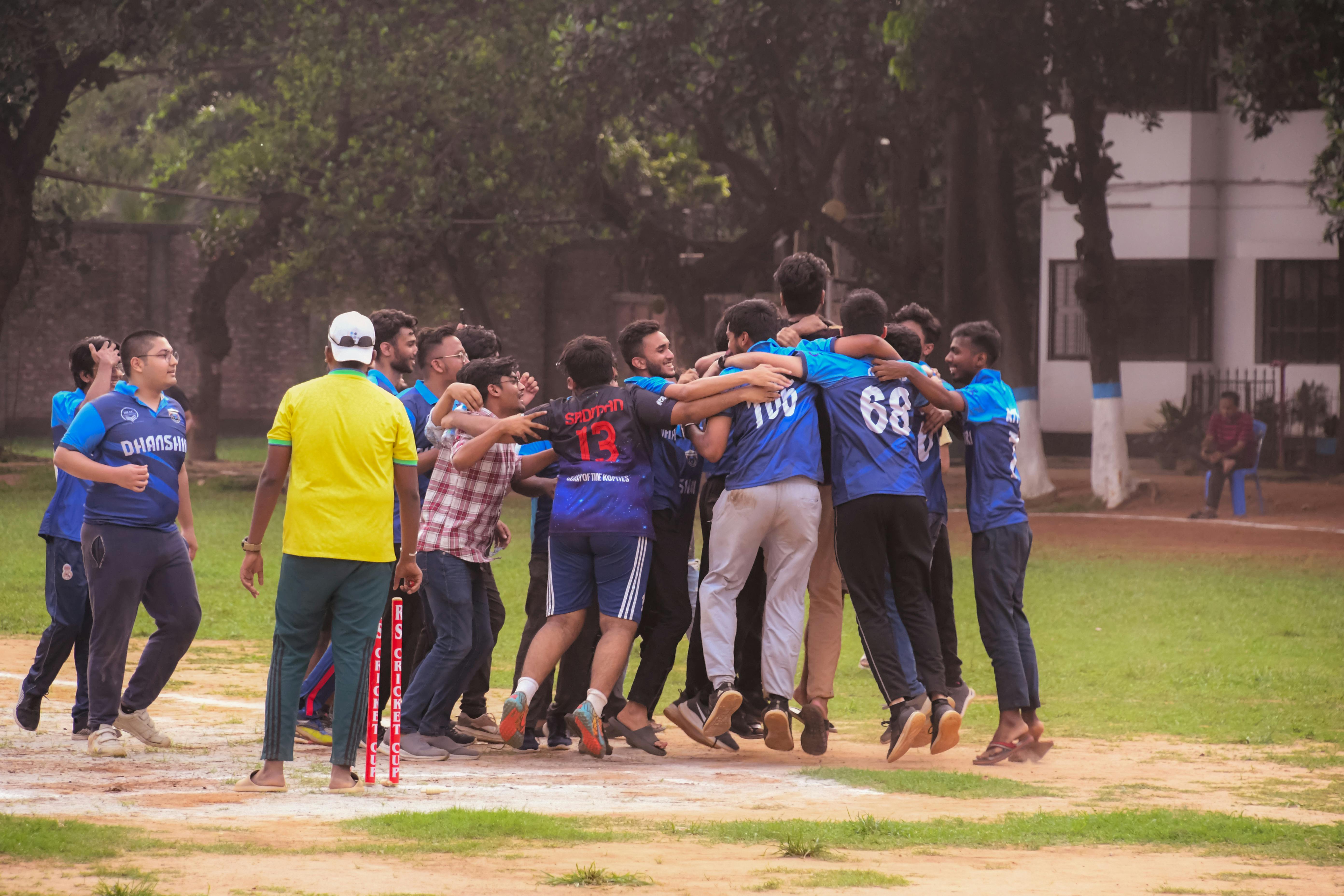 Excited group of male cricket players celebrate a win on a sports field outdoors.