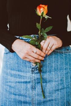 一位手持橙色玫瑰的女士，身着牛仔布服饰，尽显优雅与时尚