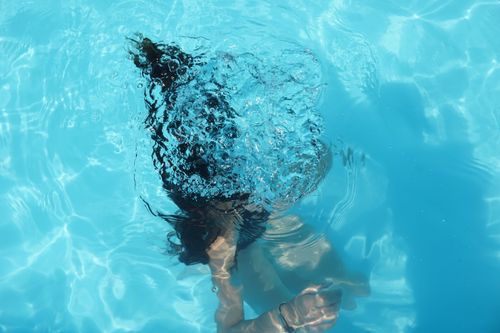 Free A woman diving underwater in a clear blue swimming pool, captured from above. Stock Photo
