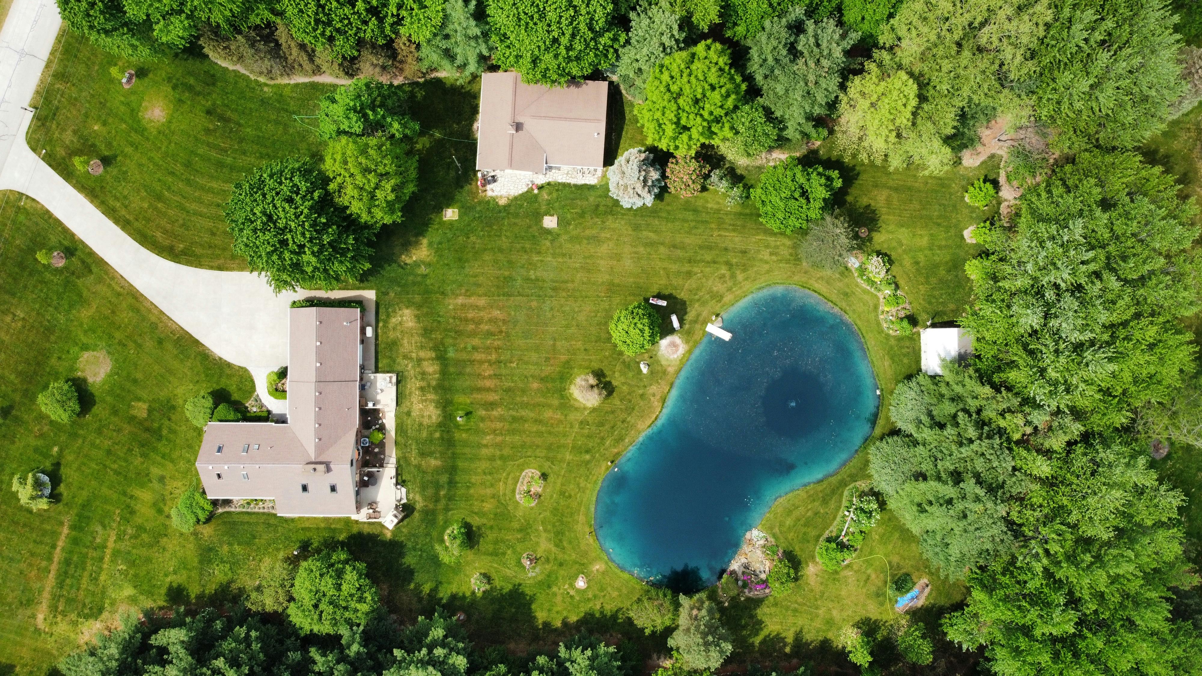 Bird's eye view of rural houses and a pond surrounded by lush greenery in Almont, Michigan.