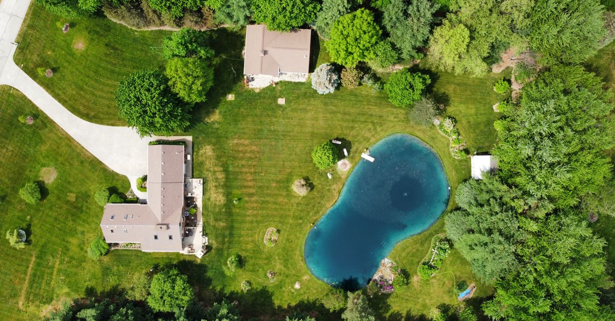 Bird's eye view of rural houses and a pond surrounded by lush greenery in Almont, Michigan.