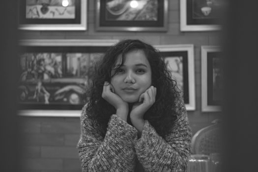 A young woman with curly hair poses in a cozy restaurant setting.