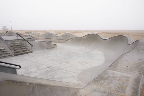 Free A deserted concrete skatepark adjacent to a sandy beach under a foggy sky. Stock Photo