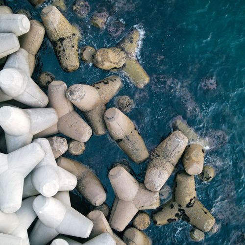 Free Concrete breakwaters protecting the coastline against the dynamic blue sea in a dramatic aerial shot. Stock Photo