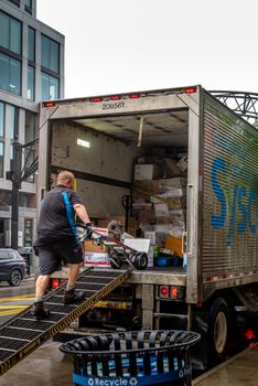 A man loads packages into a delivery truck in a modern urban area.