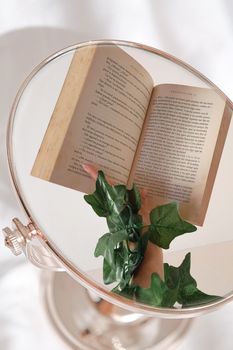 A book and leaves reflected in a circular mirror with elegant composition.