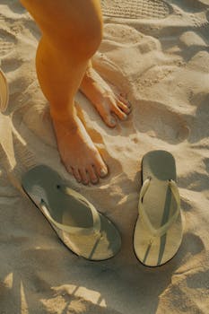 Bare feet and flip flops on sandy beach during sunny day.