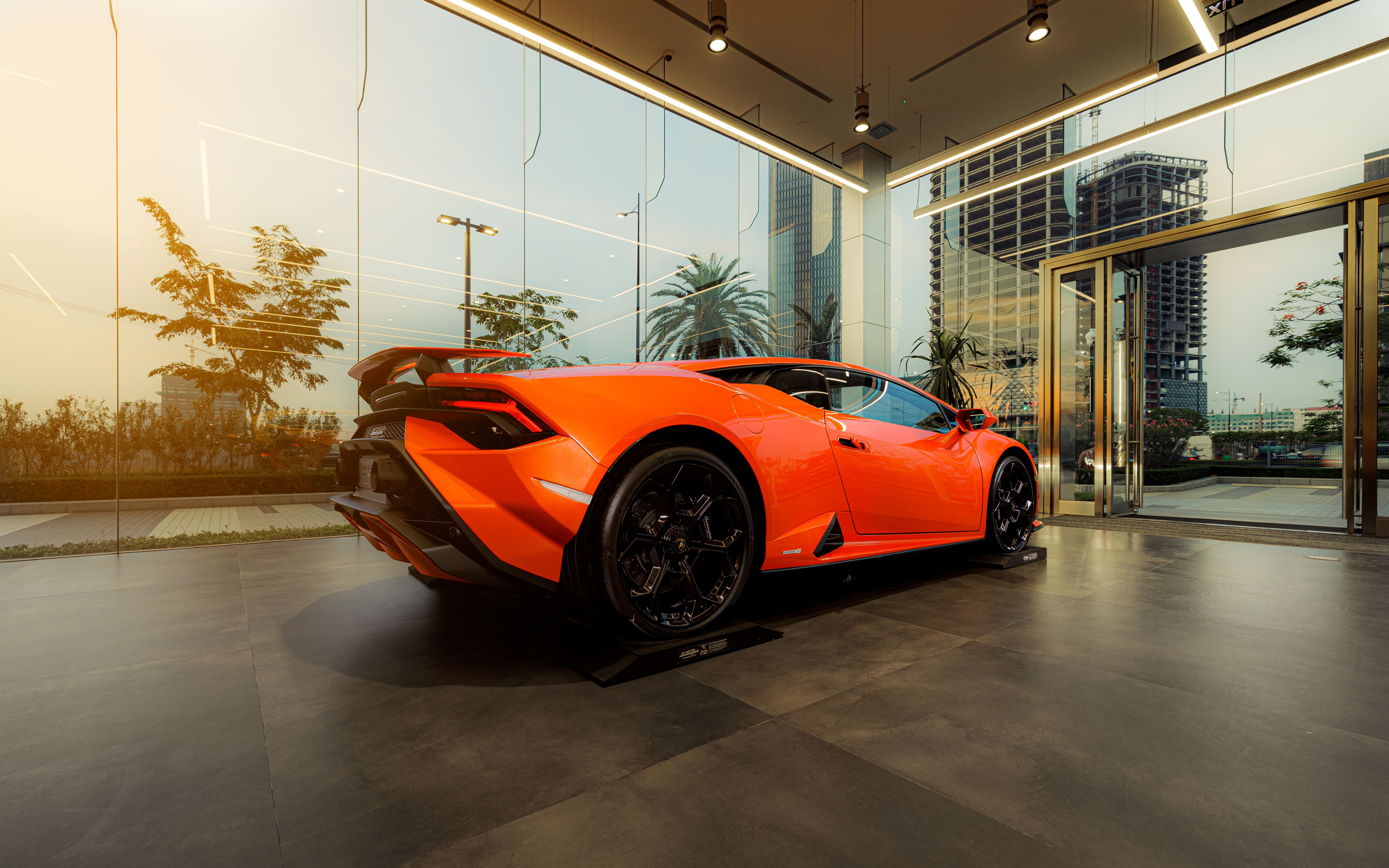 Sleek orange sports car displayed in a modern indoor showroom with glass walls.