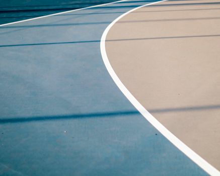 Close-up view of curved lines on an outdoor basketball court with blue and beige surfaces.