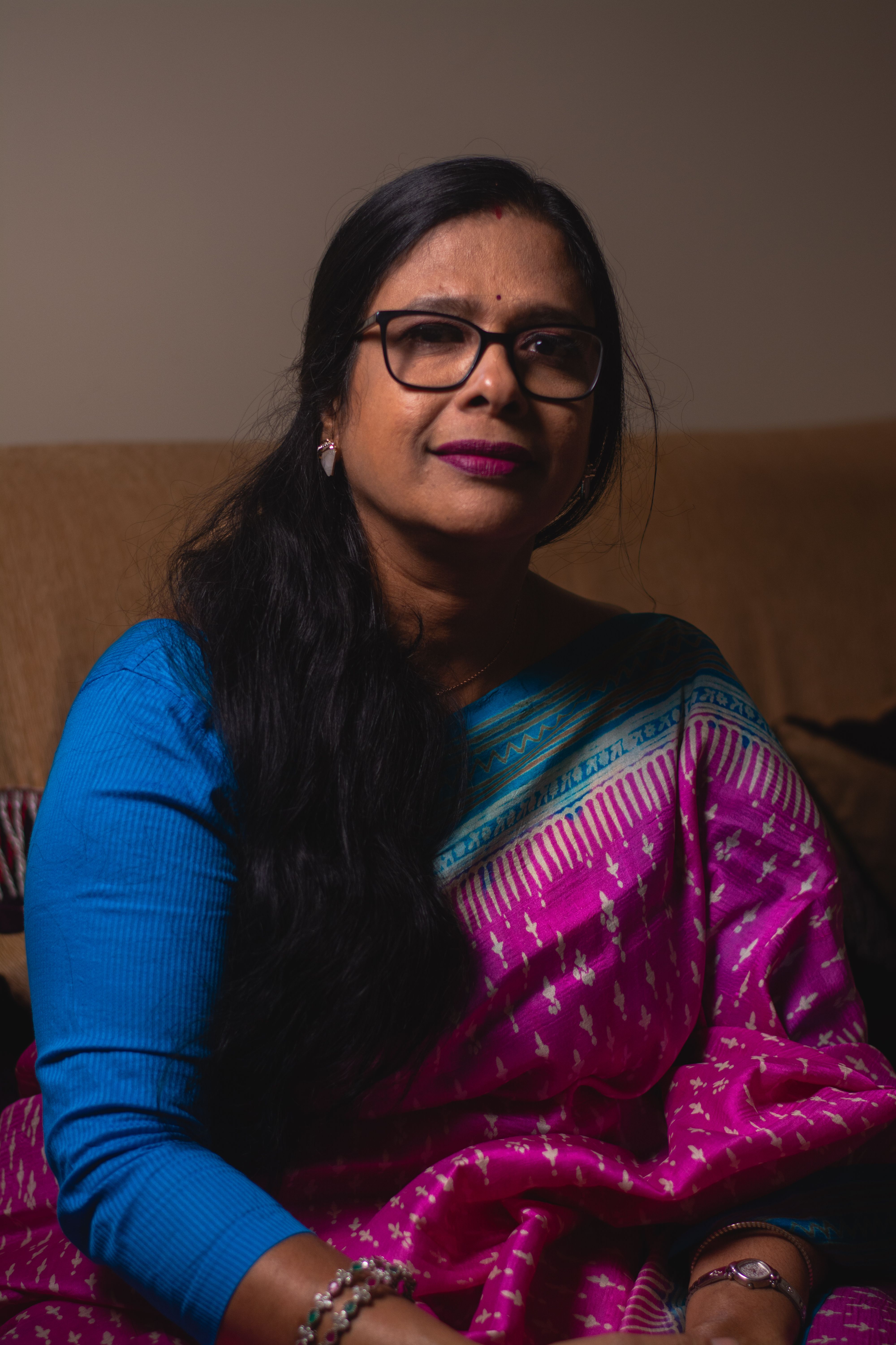 Portrait of a woman in a vibrant saree sitting indoors, exuding grace and charm.