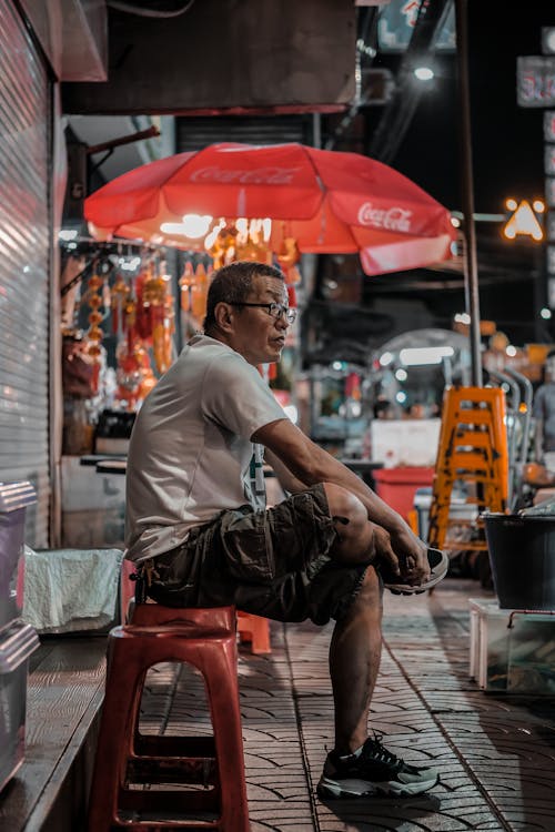 A man sitting on a stool in front of an open air market
