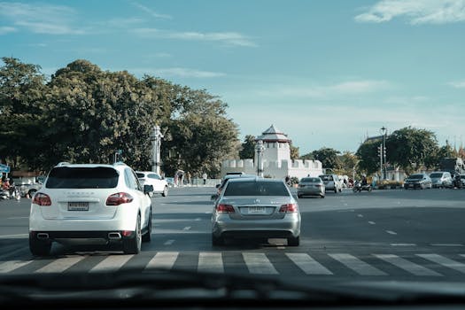 Cars driving on a city street near a historical landmark, under a clear blue sky.