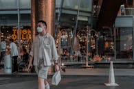 A man wearing a mask walking in a lively Bangkok street, showcasing urban life.